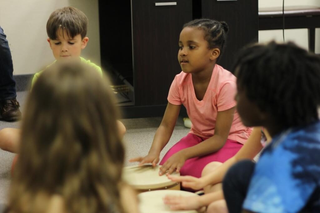 Children enjoying a drumming and singing activity during a Musikgarten group piano class. 